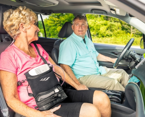 Woman using a portable oxygen concentrator in a carry bag while riding in a car